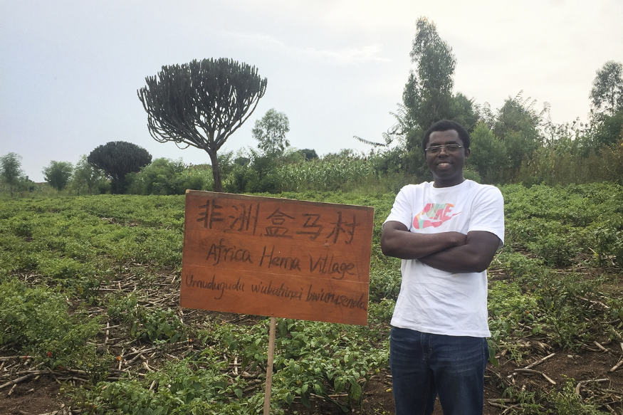 Uwizeyimana Herman poses beside the sign of the “Africa Hema Village” in Gashora, Rwanda. Source: China Daily